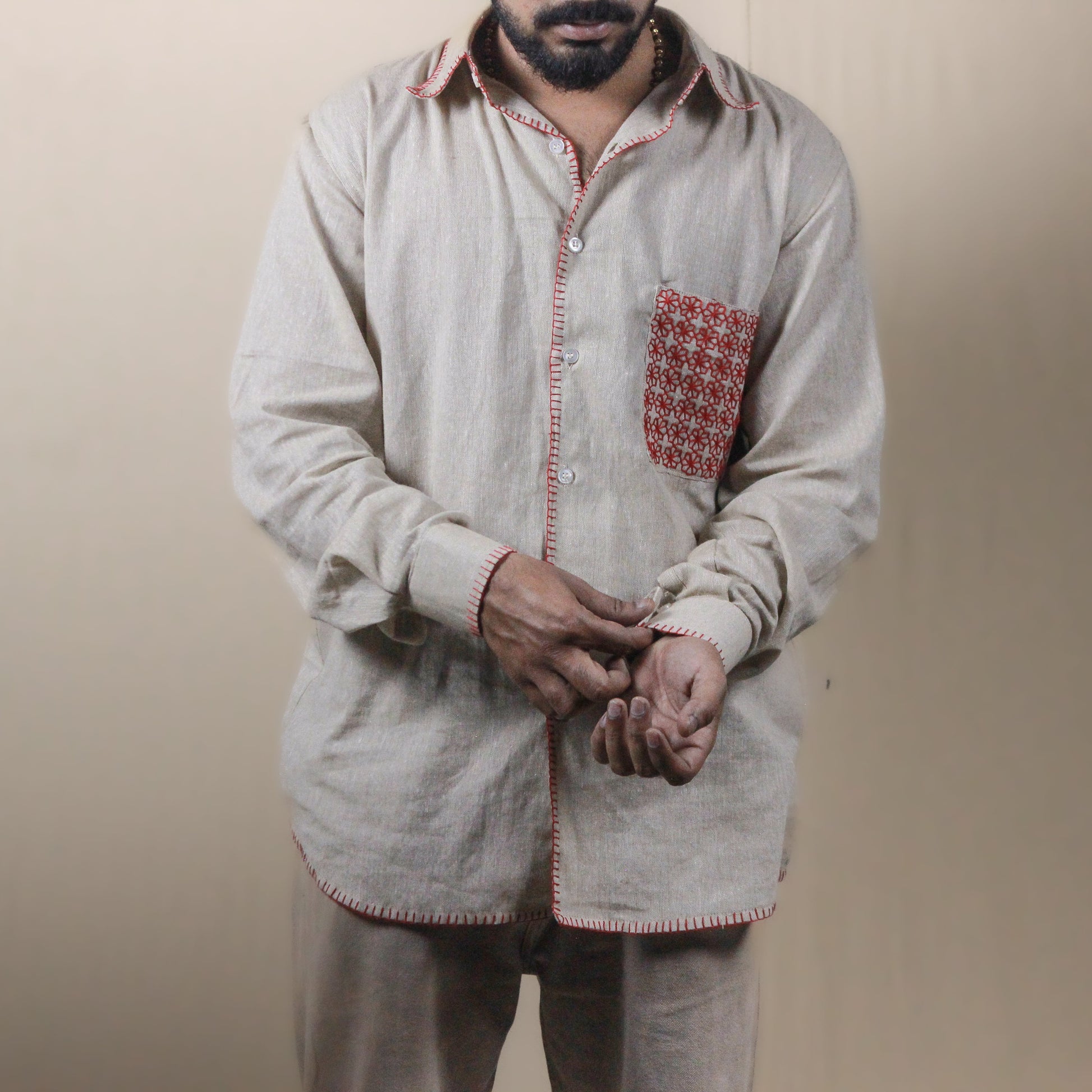 Man wearing a light-colored traditional outfit with a patterned pocket on a beige background