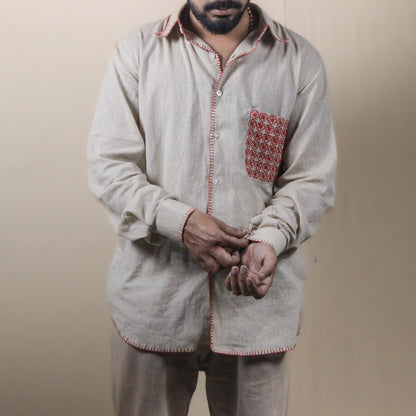 Man wearing a light-colored traditional outfit with a patterned pocket on a beige background